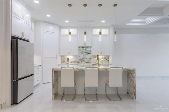 kitchen with stainless steel refrigerator, decorative light fixtures, white cabinetry, light stone countertops, and a center island with sink