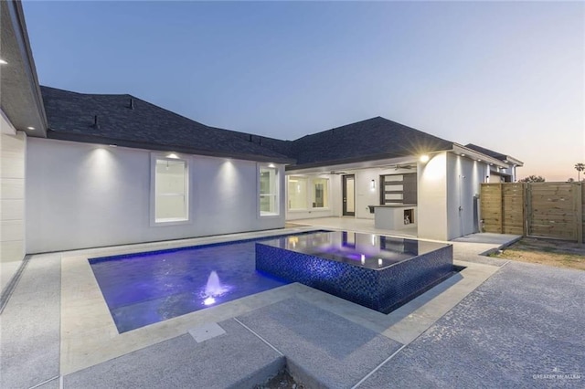 pool at dusk featuring an in ground hot tub, pool water feature, ceiling fan, and a patio