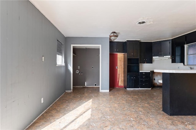 kitchen with tile counters, visible vents, dark cabinetry, under cabinet range hood, and backsplash