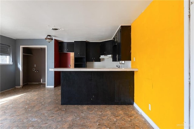 kitchen with tile counters, backsplash, a peninsula, under cabinet range hood, and baseboards