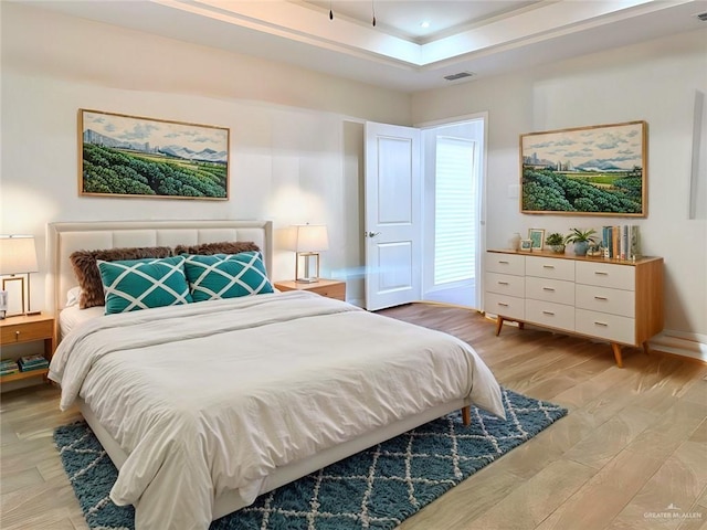 bedroom with light hardwood / wood-style floors and a tray ceiling