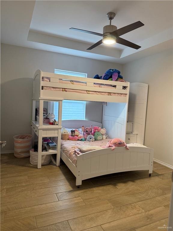 bedroom with ceiling fan, a tray ceiling, and light hardwood / wood-style flooring