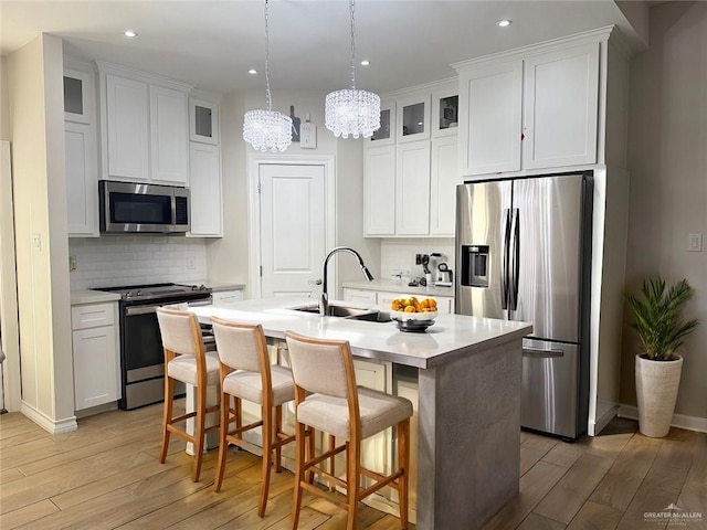 kitchen with appliances with stainless steel finishes, backsplash, white cabinetry, and an island with sink