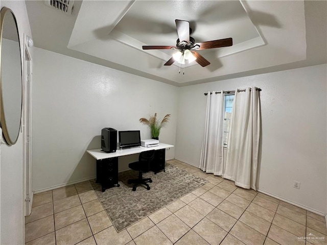 tiled office space featuring ceiling fan and a tray ceiling