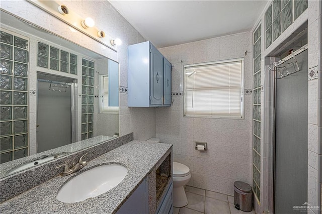 bathroom with vanity, a shower with door, tile patterned floors, toilet, and tile walls