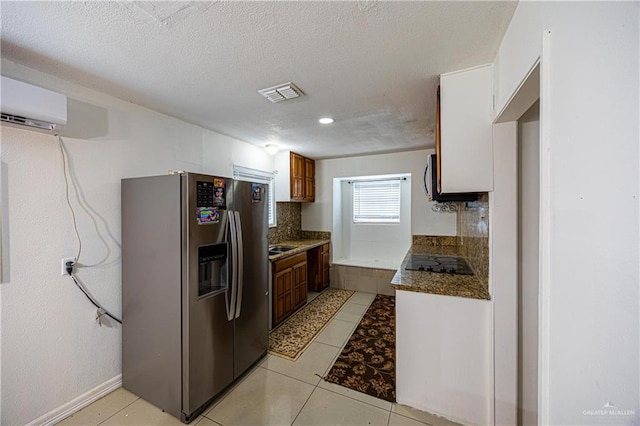 kitchen featuring stainless steel fridge, a textured ceiling, black electric cooktop, light tile patterned floors, and an AC wall unit