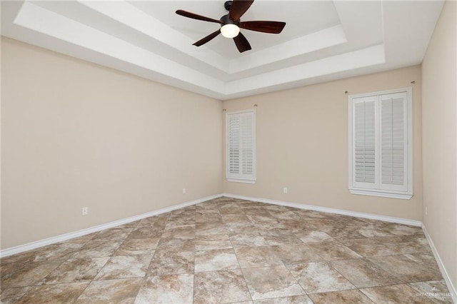 empty room with a raised ceiling, baseboards, and ceiling fan