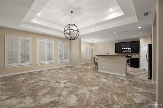 kitchen with baseboards, a chandelier, open floor plan, a tray ceiling, and stainless steel appliances