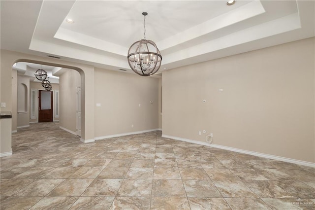 spare room with a tray ceiling, arched walkways, a notable chandelier, and baseboards