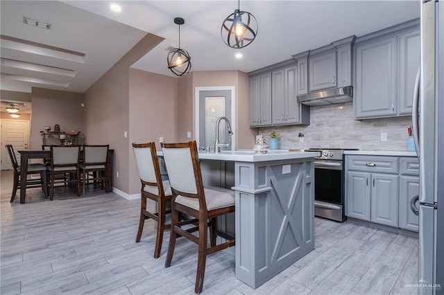 kitchen with stainless steel appliances, a kitchen island with sink, pendant lighting, and light wood-type flooring