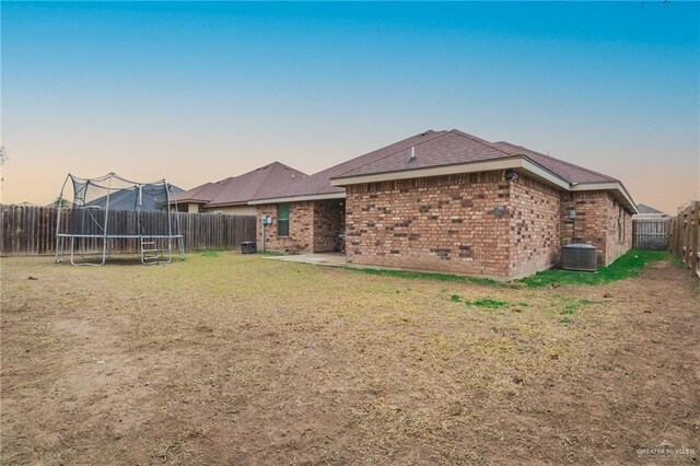 back house at dusk with a patio, a trampoline, and a lawn