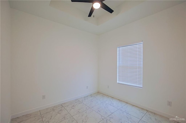 spare room with a ceiling fan, a tray ceiling, baseboards, and marble finish floor