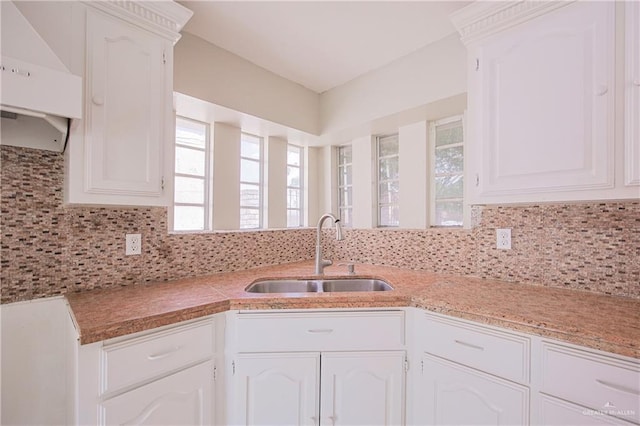 kitchen with light countertops, range hood, white cabinets, and a sink