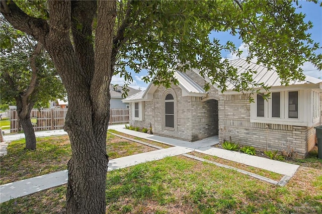 view of front of home with metal roof, brick siding, a front lawn, and fence