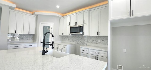 kitchen with stainless steel microwave, light stone counters, decorative backsplash, and a sink