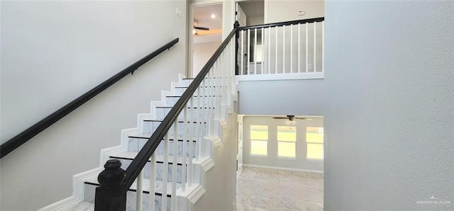 stairs featuring a ceiling fan, baseboards, and a towering ceiling