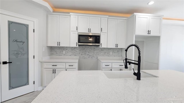 kitchen featuring white cabinets, light stone counters, a sink, stainless steel microwave, and tasteful backsplash