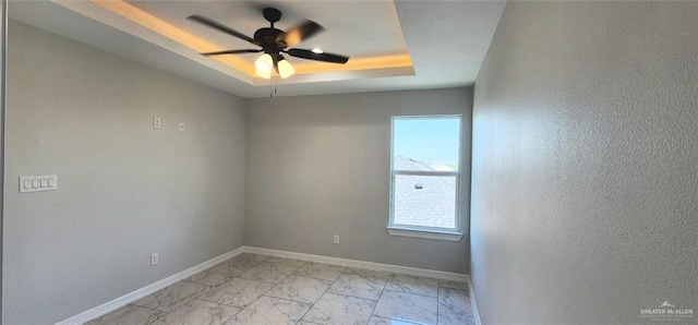 empty room featuring a tray ceiling, baseboards, a ceiling fan, and marble finish floor