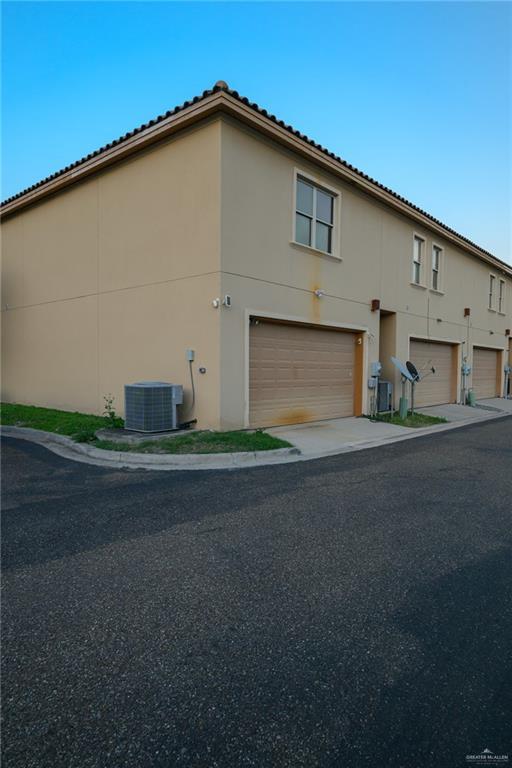 view of side of home featuring central air condition unit, an attached garage, and stucco siding