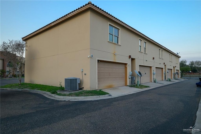 view of side of home with a garage, stucco siding, and central air condition unit