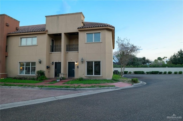 view of front of house with a balcony, a tiled roof, and stucco siding