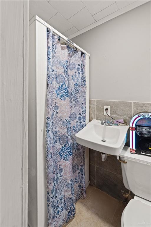 bathroom with toilet, tile patterned floors, tile walls, and sink