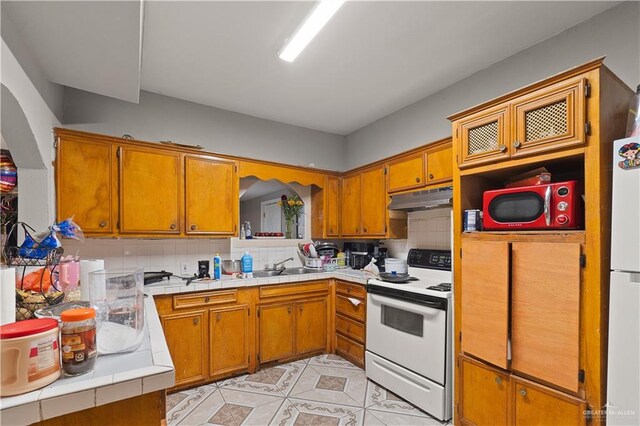 kitchen with sink, white appliances, tile countertops, and backsplash