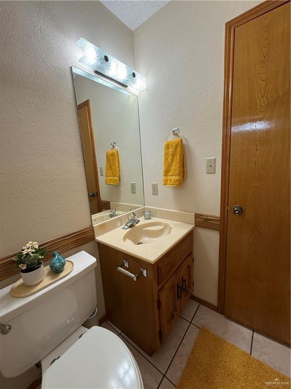 2303 Viola St, Mission, TX 78574 - half bath with vanity, a textured wall, toilet, a textured ceiling, and tile patterned floors