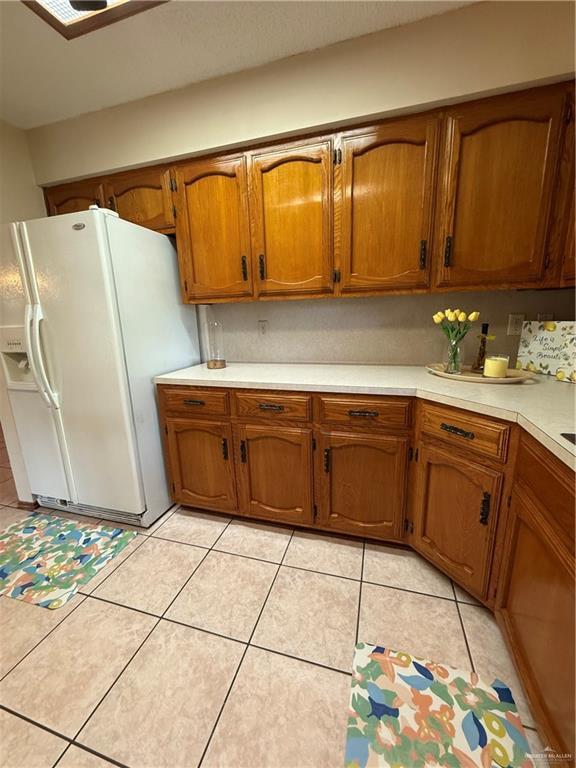 2303 Viola St, Mission, TX 78574 - kitchen with brown cabinetry, light countertops, light tile patterned floors, and white fridge with ice dispenser