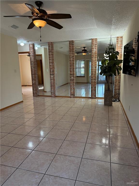 2303 Viola St, Mission, TX 78574 - unfurnished room featuring light tile patterned flooring, a textured ceiling, brick wall, a ceiling fan, and visible vents