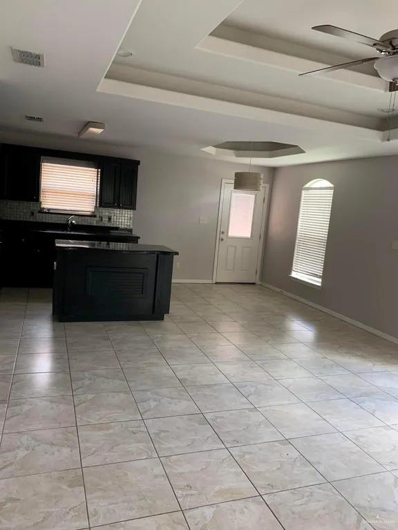 kitchen with light tile patterned floors, a raised ceiling, ceiling fan, and a center island