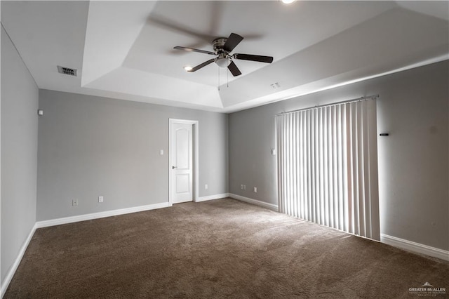 carpeted empty room with visible vents, a tray ceiling, ceiling fan, and baseboards
