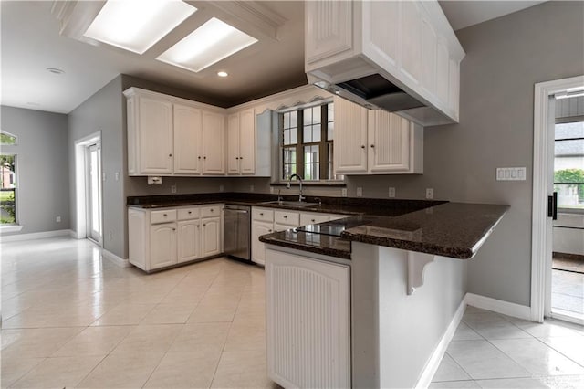 kitchen featuring a breakfast bar, a peninsula, light tile patterned floors, stainless steel dishwasher, and a sink
