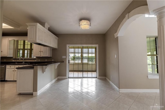 kitchen featuring arched walkways, dishwasher, a sink, a peninsula, and a kitchen bar