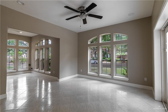 tiled spare room featuring baseboards and ceiling fan