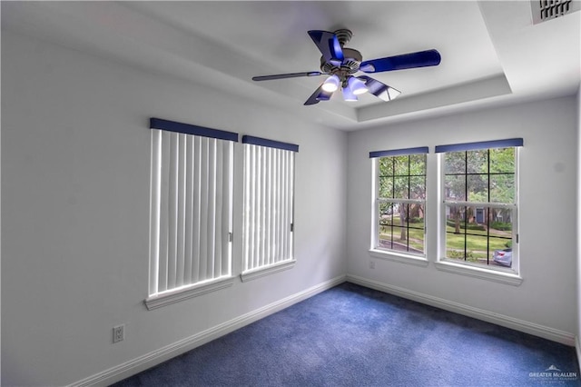 carpeted empty room featuring a tray ceiling, ceiling fan, baseboards, and visible vents