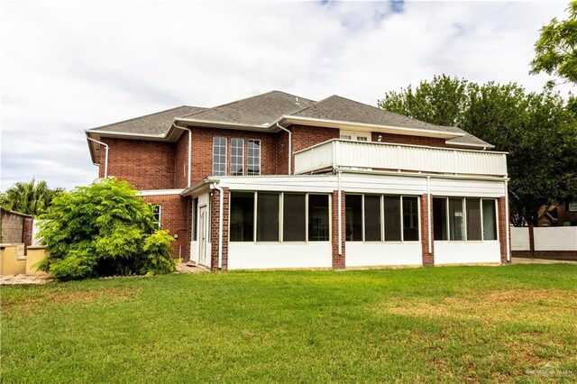 back of property featuring brick siding, a sunroom, a lawn, and a balcony