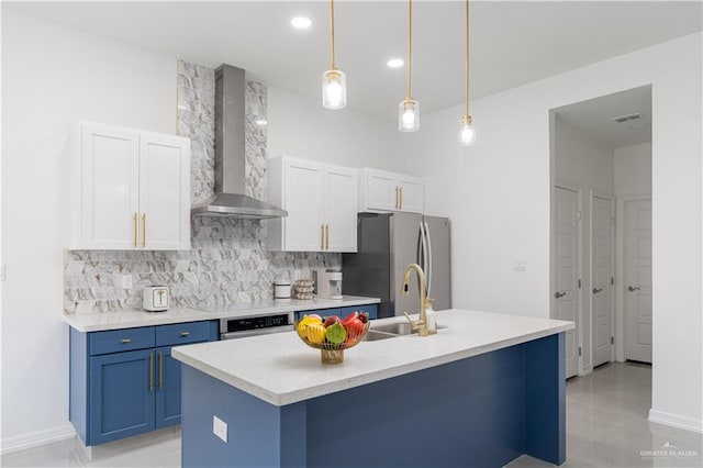 kitchen with wall chimney exhaust hood, stainless steel appliances, hanging light fixtures, an island with sink, and white cabinets