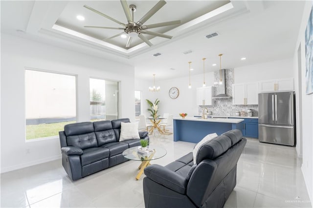 tiled living room with ceiling fan with notable chandelier, sink, and a tray ceiling