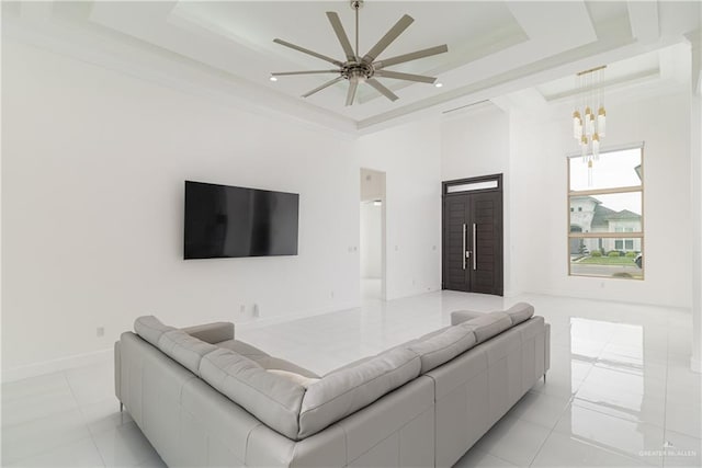 living room with ceiling fan with notable chandelier, crown molding, a raised ceiling, and light tile patterned flooring