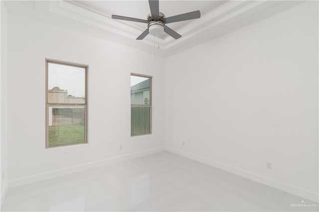 tiled empty room featuring ceiling fan and a raised ceiling