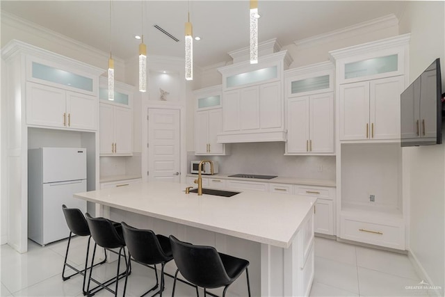 kitchen with white refrigerator, white cabinets, hanging light fixtures, and an island with sink