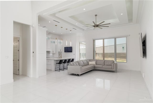 tiled living room with ceiling fan, a raised ceiling, and sink