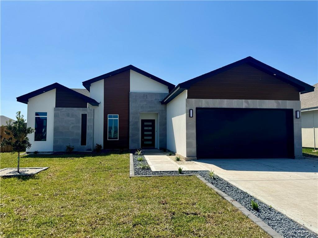 view of front of home featuring driveway, stucco siding, a front lawn, a garage, and stone siding