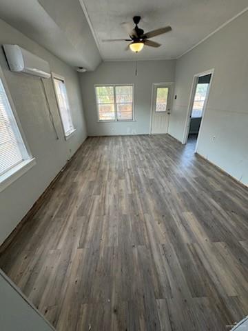 unfurnished living room featuring a wall mounted AC, wood finished floors, and a ceiling fan
