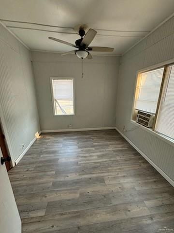 spare room featuring crown molding, baseboards, wood finished floors, a ceiling fan, and cooling unit