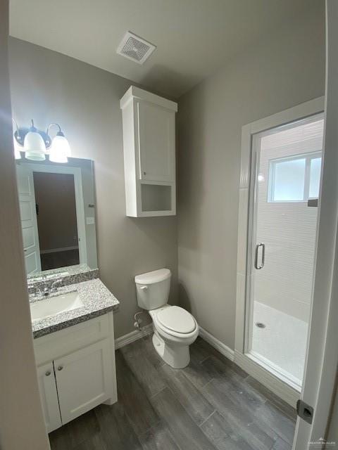 bathroom featuring hardwood / wood-style floors, vanity, toilet, and a shower with shower door