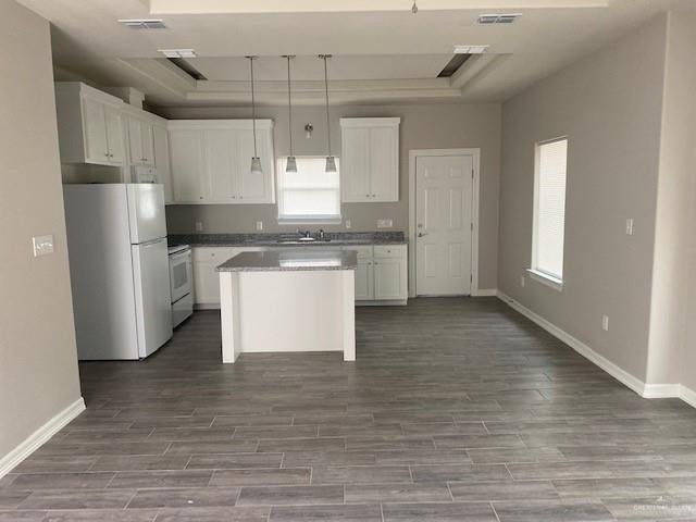 kitchen with white appliances, a kitchen island, hardwood / wood-style flooring, white cabinetry, and hanging light fixtures