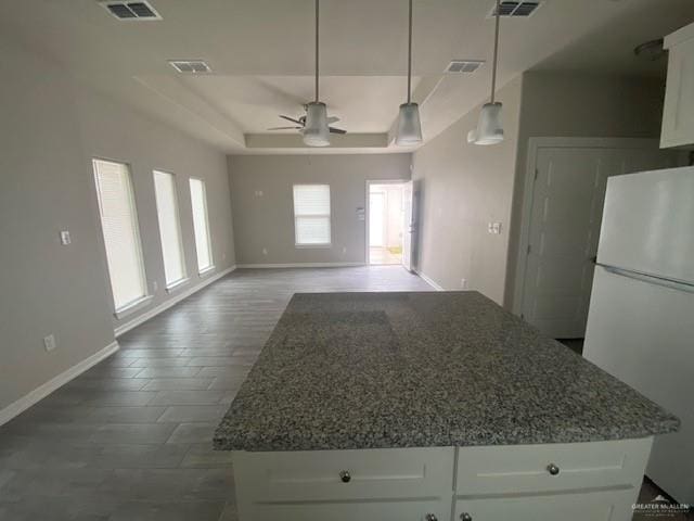 kitchen featuring white cabinetry, ceiling fan, hanging light fixtures, dark stone countertops, and white fridge