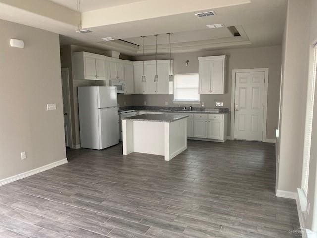 kitchen with white appliances, a tray ceiling, white cabinets, hardwood / wood-style floors, and a kitchen island